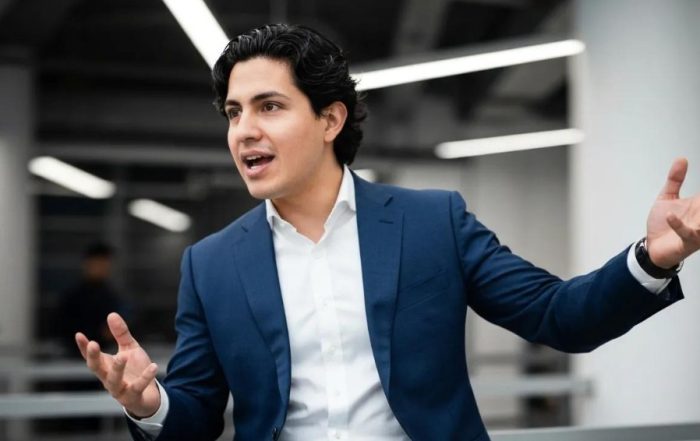 Man in a blue suit gesturing while speaking, representing effective communication and engagement, relevant to discussions about understanding client personality types in the B.A.N.K. system.